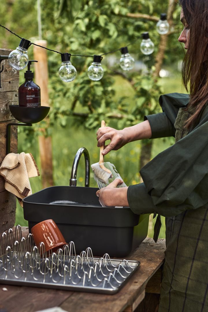 Outdoor Küche selber bauen: Eine Frau wäscht Geschirr in ihrer Outdoor-Küche mit einer tragbaren Waschschüssel von Brabantia ab. 