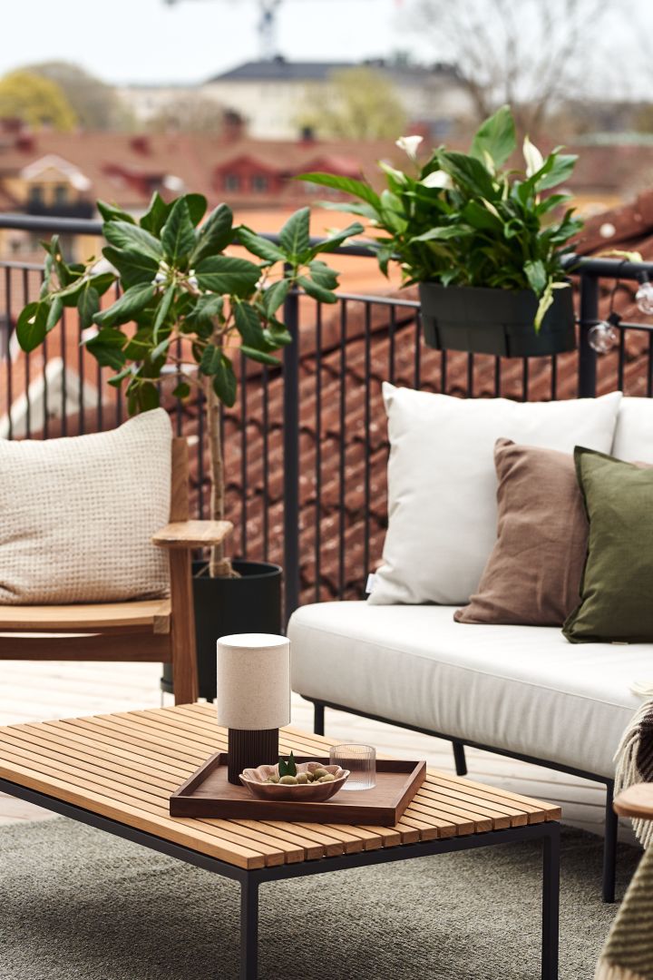 Hier sehen Sie einen gemütlich eingerichteten Balkon, bestehend aus einem Sofa, Stühlen, einem Couchtisch und zahlreichen Pflanzen.