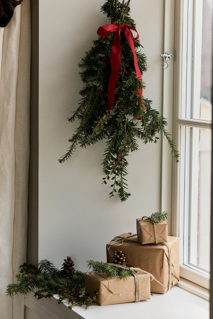 Weihnachtsdekoration basteln mit Tannengrün: Hier sehen Sie ein Bündel Tannenzweige in einem Fenster aufgehängt, auf dem Fensterbrett darunter liegen einige kleinere Geschenke.