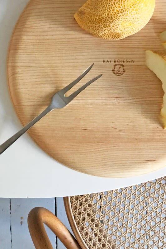 Hier sehen Sie das Serviertablett aus Holz von Kay Bojesen auf einem Tisch, darauf eine Gabel und eine Honigmelone.