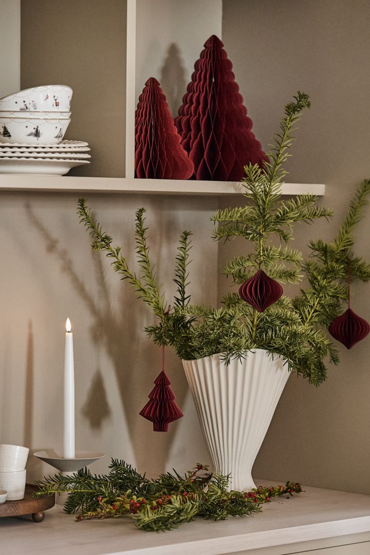 Weihnachtsdekoration basteln mit Tannengrün: Hier sehen Sie Tannenzweige in der Fountain Vase von ferm LIVING, dekoriert mit weihnachtlichen Anhängern von Scandi Living auf einer Küchenanrichte.