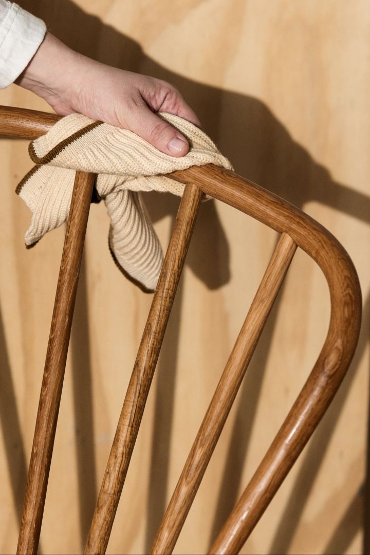 Gartenmöbel aus Teak pflegen: Hier sehen Sie eine Hand, die einen Stuhl aus Teakholz mit einem Tuch reinigt.