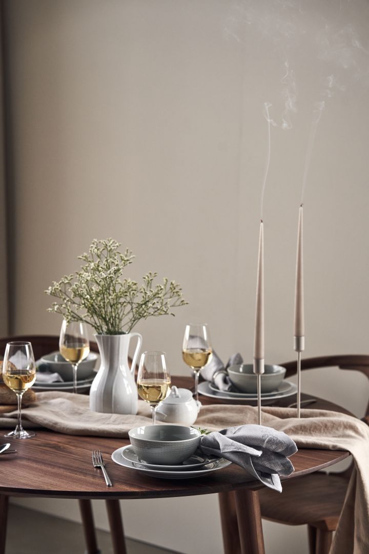 Ein festlich gedeckter Tisch mit Kerzen, Wiesenblumen in einer Karaffe von Pli Blanc und Swedish Grace-Porzellan in Weiß und Grau. 