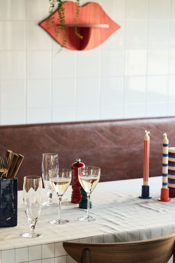 Hier sehen Sie die Chateau-Weißweingläser von Kosta Boda auf einem gedeckten Tisch mit bunten HAY-Kerzenhaltern auf dem Tisch. 