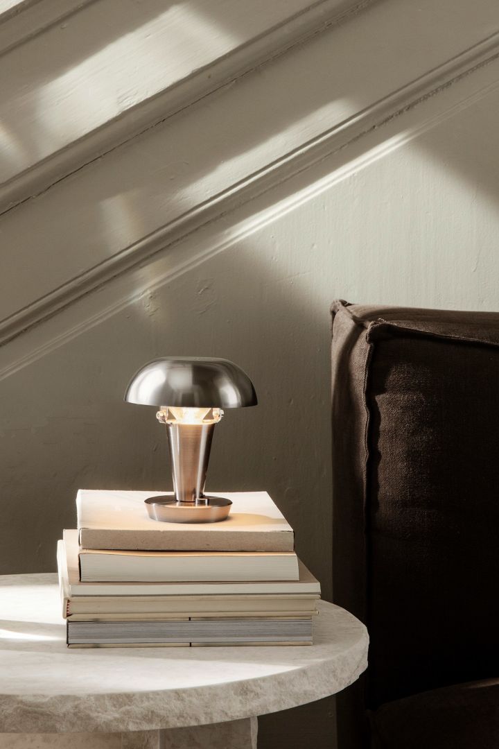 Eine weitere trendige Pilzlampe ist die Tischleuchte Tiny von ferm LIVING, die auf dem Beistelltisch oder auf der Fensterbank zu einem stilvollen Einrichtungsdetail in Ihrem Zuhause wird. Hier steht sie auf einem Stapel Bücher, welche auf einem Marmortisch platziert sind.