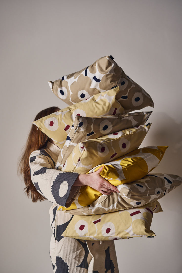 Eine Frau trägt einen Stapel Unikko-Kissen in ihren Armen.