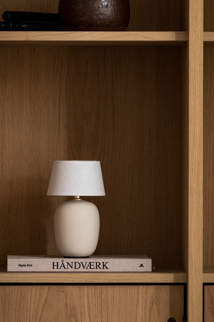 Entdecken Sie den Trend der Pilzlampe: Hier sehen Sie die tragbare Torso Tischleuchte von Audo Copenhagen in einem Bücherregal aus Holz. 