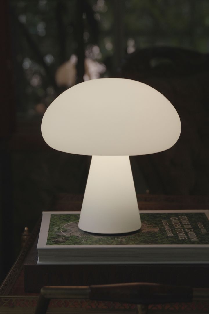 Entdecken Sie die angesagtesten Pilzlampen: Hier sehen Sie die tragbare Tischleuchte Obello aus Milchglas von Gubi, die draußen im Dunkeln auf einem Magazin steht. 